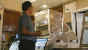 Man in a store, facing away, with a display case and point-of-sale system in front of him
