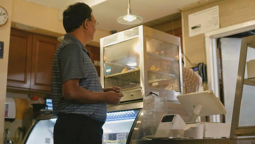 Man in a store, facing away, with a display case and point-of-sale system in front of him
