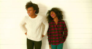 Two young women laughing, one in a white sweater, the other in a red and black plaid shirt