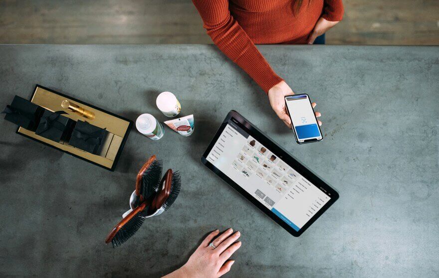 Overhead view of a customer paying with a smartphone at a retail counter with a POS tablet