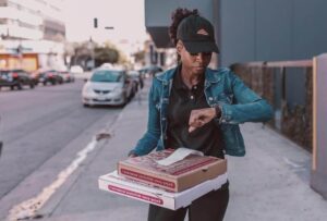 Pizza delivery person checks watch, holding two pizza boxes with paper receipts