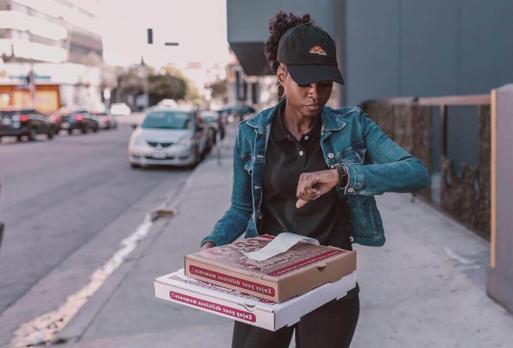 Pizza delivery person checks watch, holding two pizza boxes with paper receipts