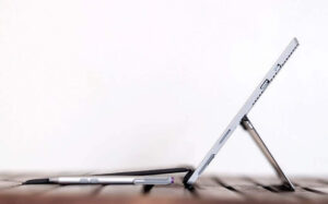 A silver tablet with a kickstand and a stylus on a wooden surface