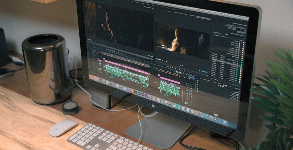 Desktop computer displaying video editing software, with a Mac Pro and keyboard on a wooden desk