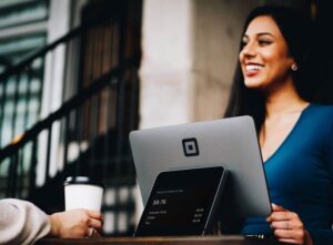 Smiling woman at a cafe counter with a Square POS system and a customer holding coffee
