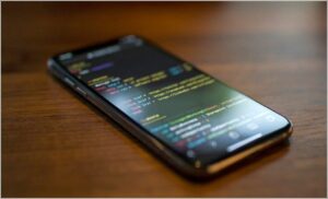 Smartphone displaying colorful code on a dark screen, resting on a wooden table