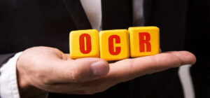 Hand holding three yellow blocks spelling "OCR" against a dark background