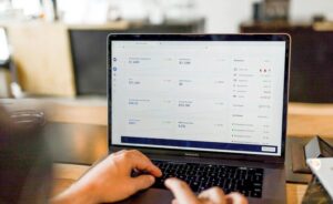 Hands type on a MacBook Pro displaying financial data and charts, with a phone nearby