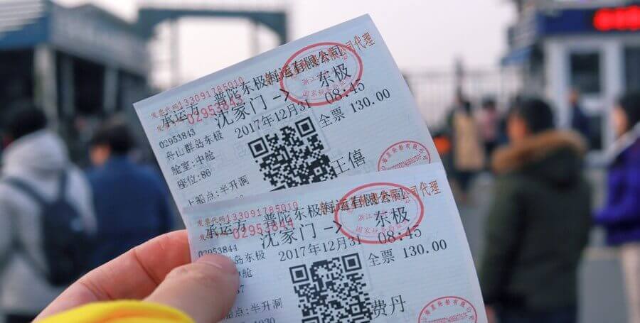 Two ferry tickets for Dongji Island, China, held by a hand, with blurred people in the background