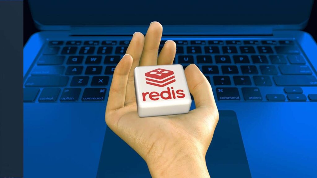 Hand holding a Redis logo block over a blue laptop keyboard
